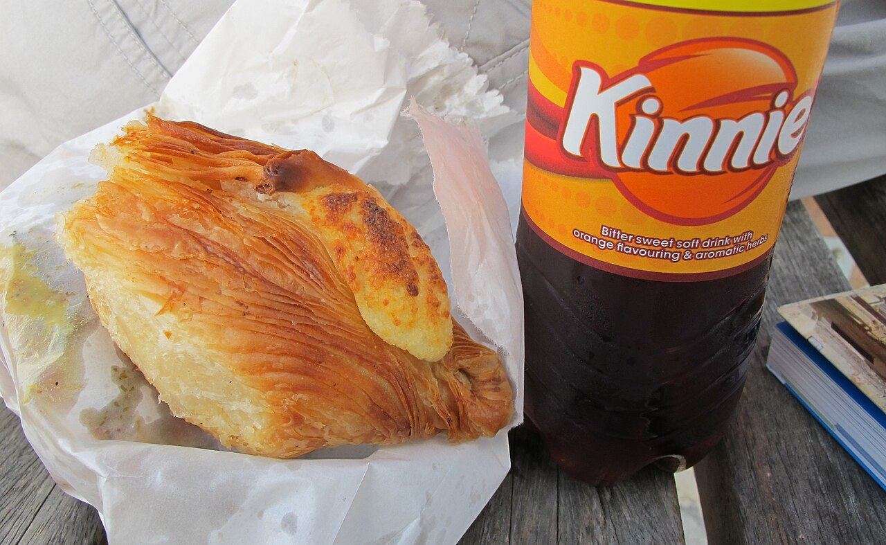 A pastizz in its paper bag next to a bottle of Kinnie